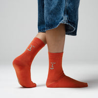 Person wearing orange socks with a subtle design, paired with blue jeans on a light gray background