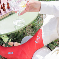 Person holding a glass of spritz with lemon outdoors, wearing red socks with 'LEIHO' branding.