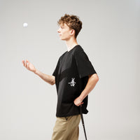 Person standing on a green mat with a golf club, wearing a black t-shirt and beige shorts.