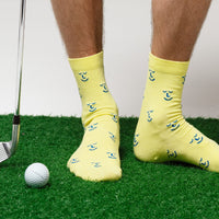 Person wearing yellow socks with a golf club and ball on a green surface